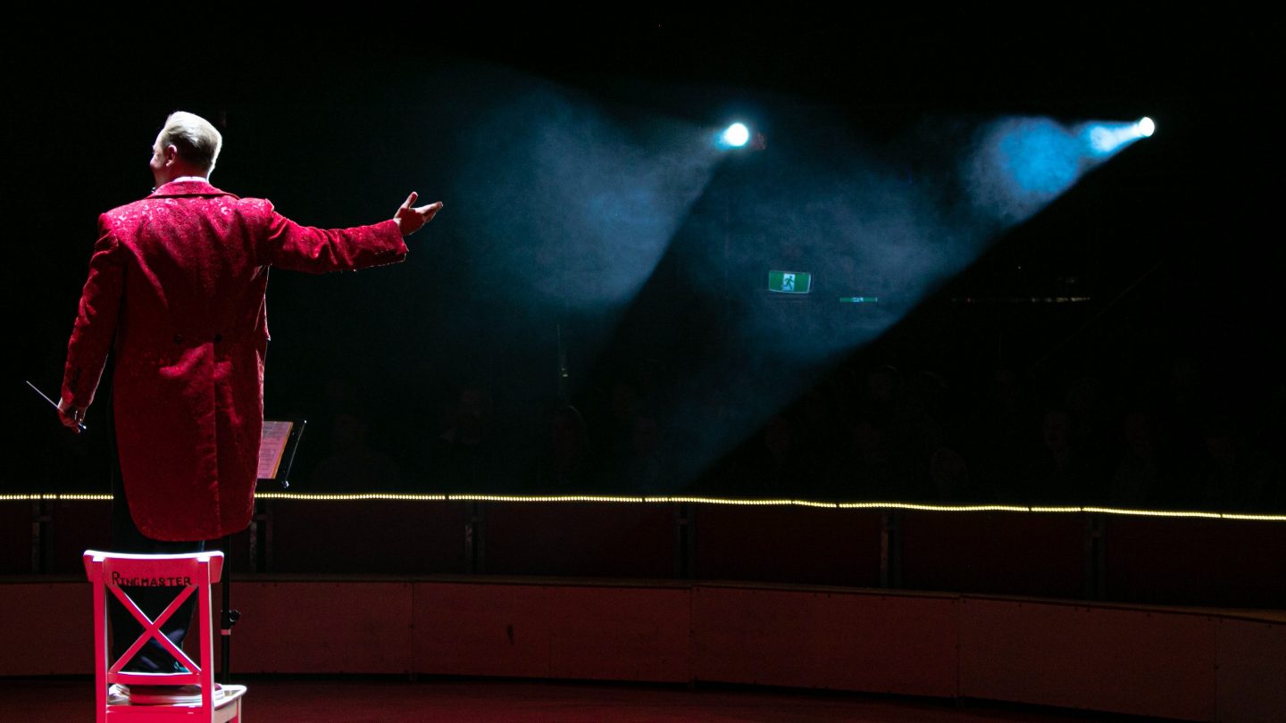 An orchestra conductor in a red tailcoat receiving applause at the end of a performance.