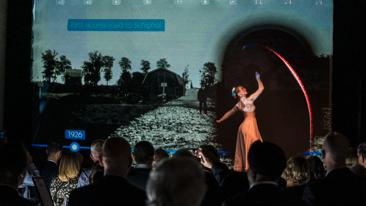 A ribbon dancer in a white dress behind a transparent screen that is showing content of a timeline.