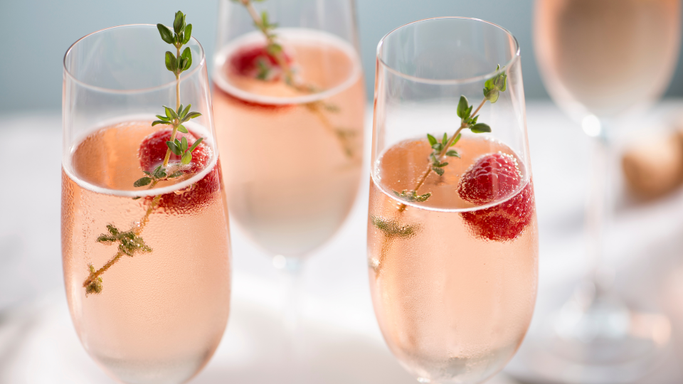 three prosecco style glasses with raspberries and a pink drink inside