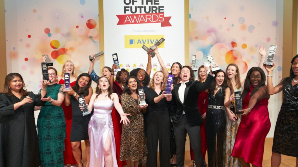 A group of women in black tie outfits cheer, holding the awards they have won in the air